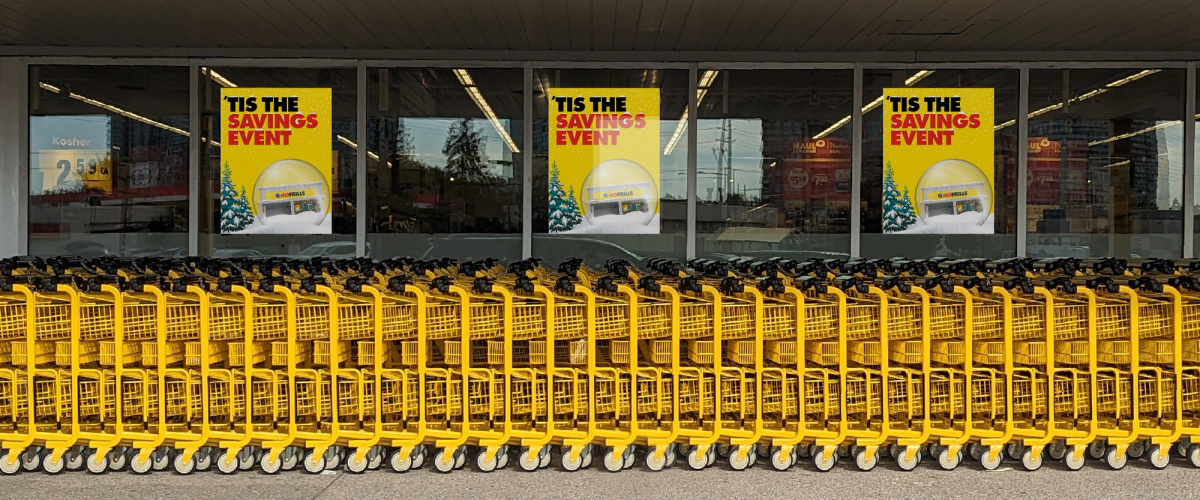 Rows of yellow No Frills shopping carts outside a store window with "Tis the Savings Event" posters