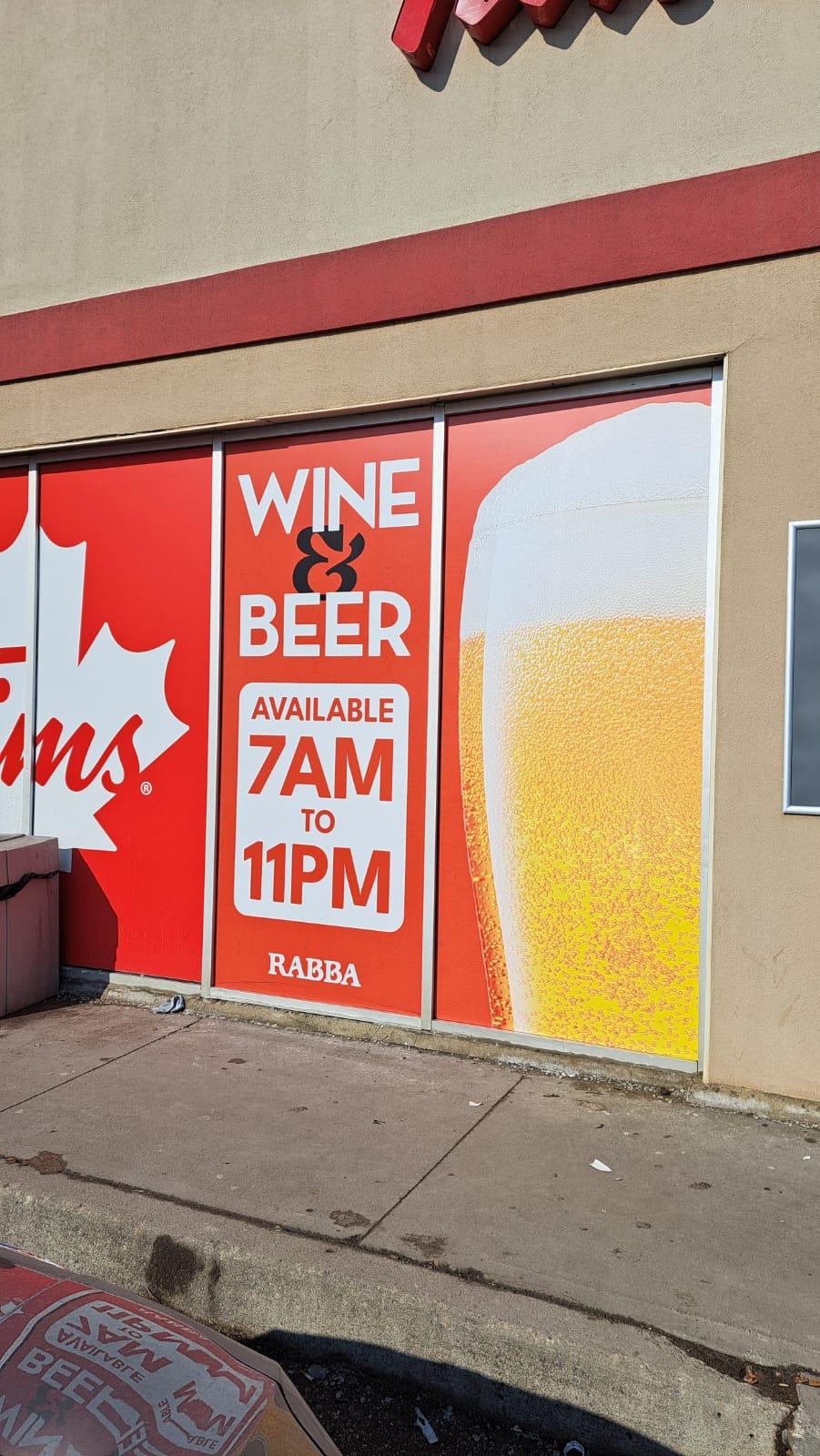 Rabba storefront window graphics reading Wine and Beer, available 7AM to 11PM, beside a full-height glass of beer