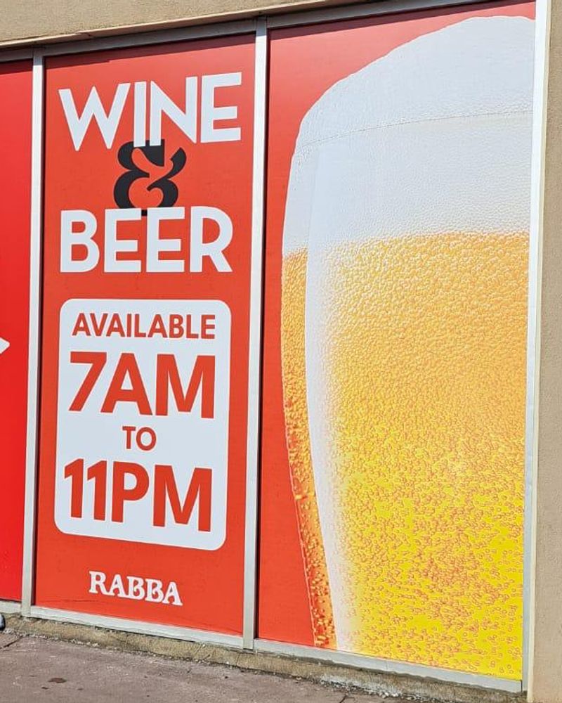 Rabba storefront window graphics reading Wine and Beer, available 7AM to 11PM, beside a full-height glass of beer