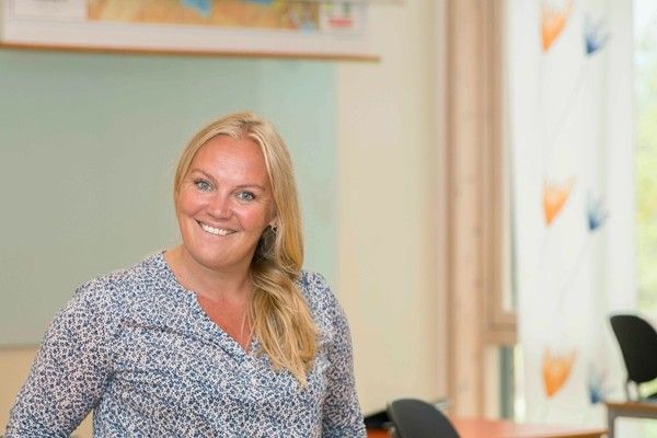 Foto, en smilende lærerinne foran tavlen i klasserommet.