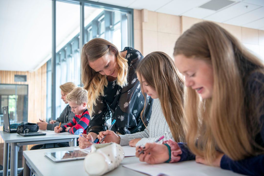 Foto, en lærer hjelper to ungdommer som bygger en liten drone med hjul.