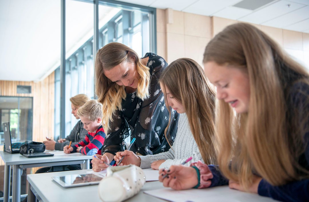 Foto, en lærer hjelper to ungdommer som bygger en liten drone med hjul.