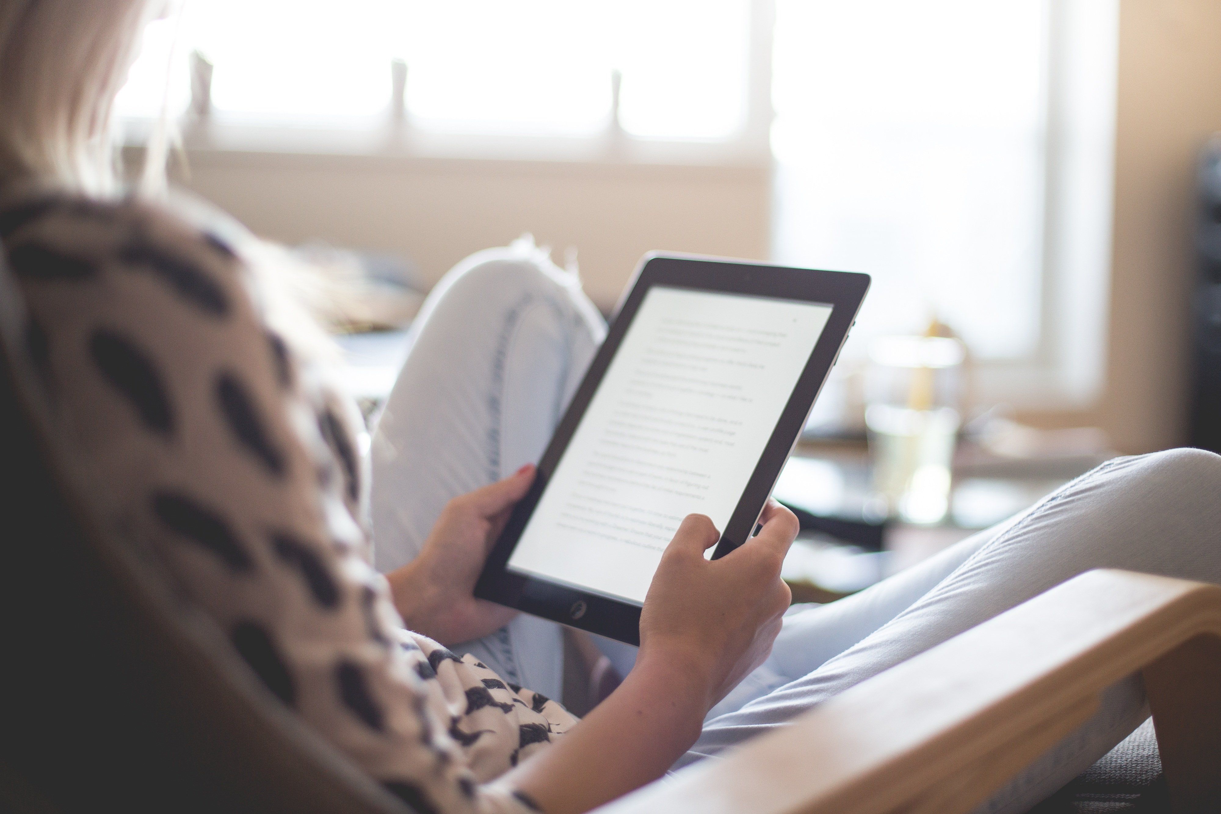 Kvinne som sitter i stol og holder en kindle i hånden.