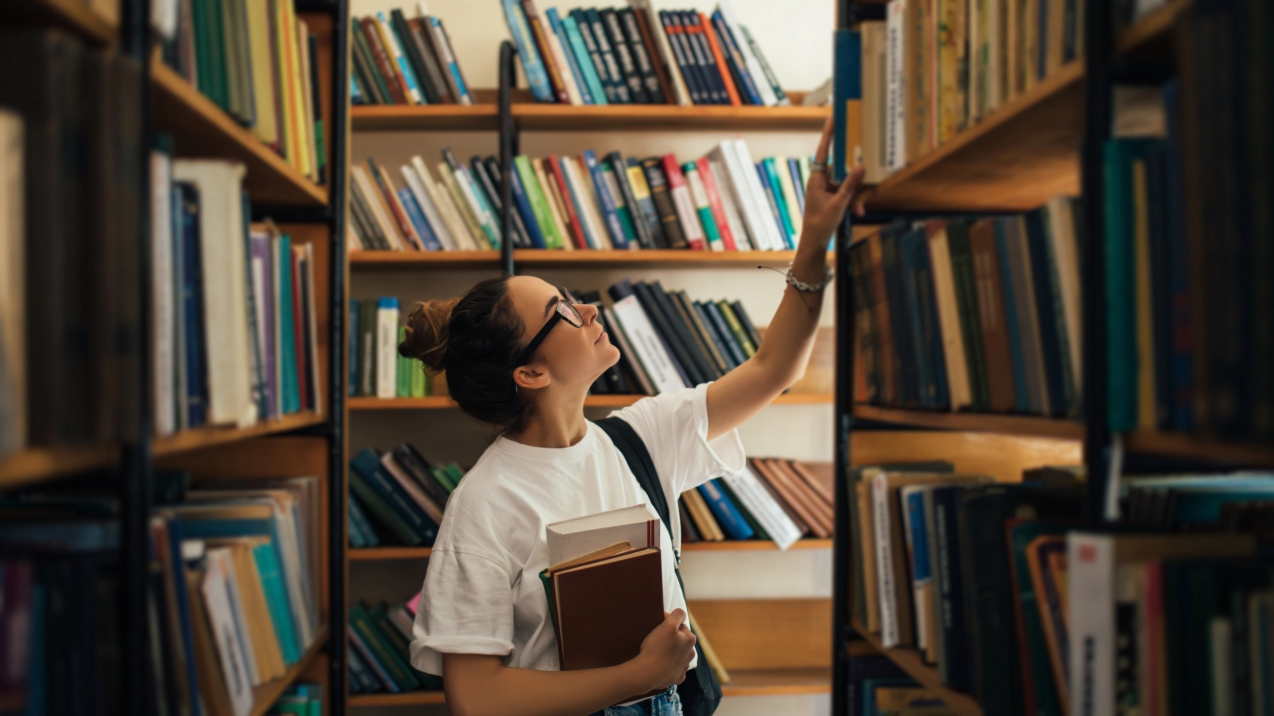 En student som holder pensumbøker i hånden og leter etter bøker på biblioteket.