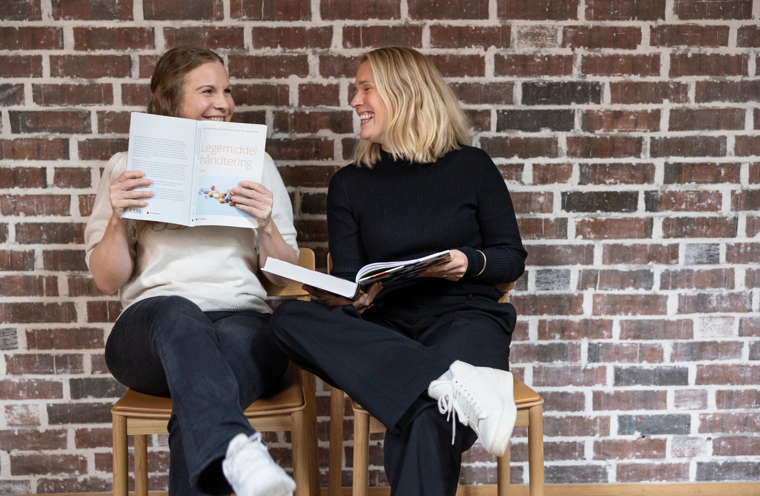 To fagredaktører i Gyldendal Akademisk sitter ned og holder to pensumbøker i hånden og smiler til hverandre.
