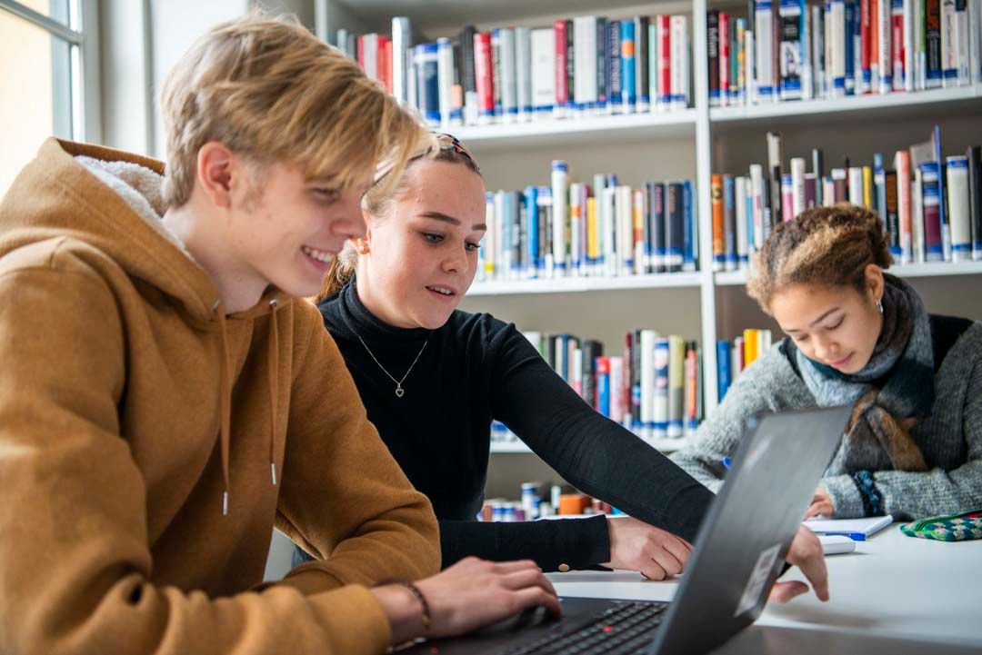 Foto, tre unge voksne som sitter ved ett bord og jobber. To fokuserer på en laptop, mens den siste sitter med en skriveblokk.
