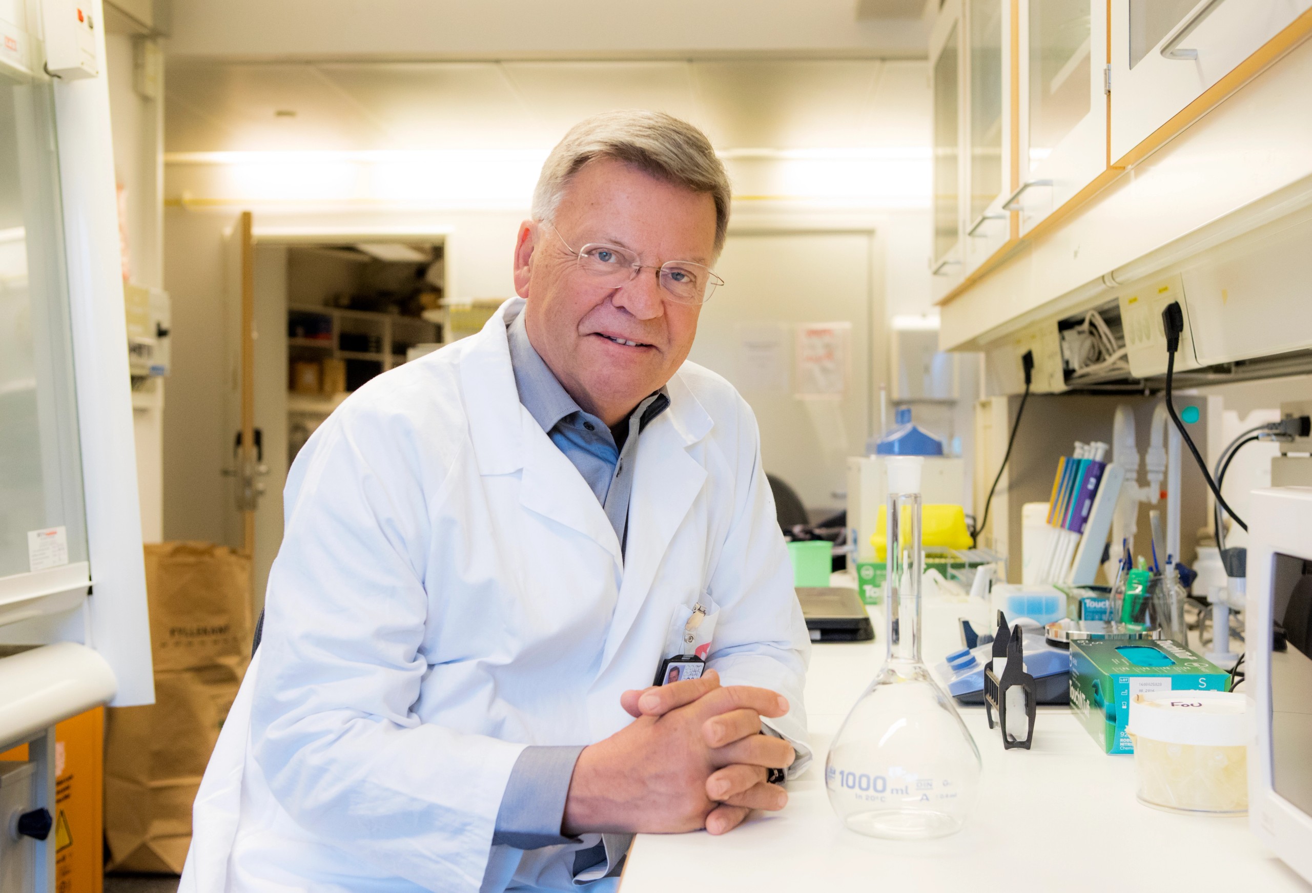 Foto av Torleiv Rognum. Han har labfrakk på seg, og sitter vendt mot kamera mens han lener seg på en laboratoriebenk.