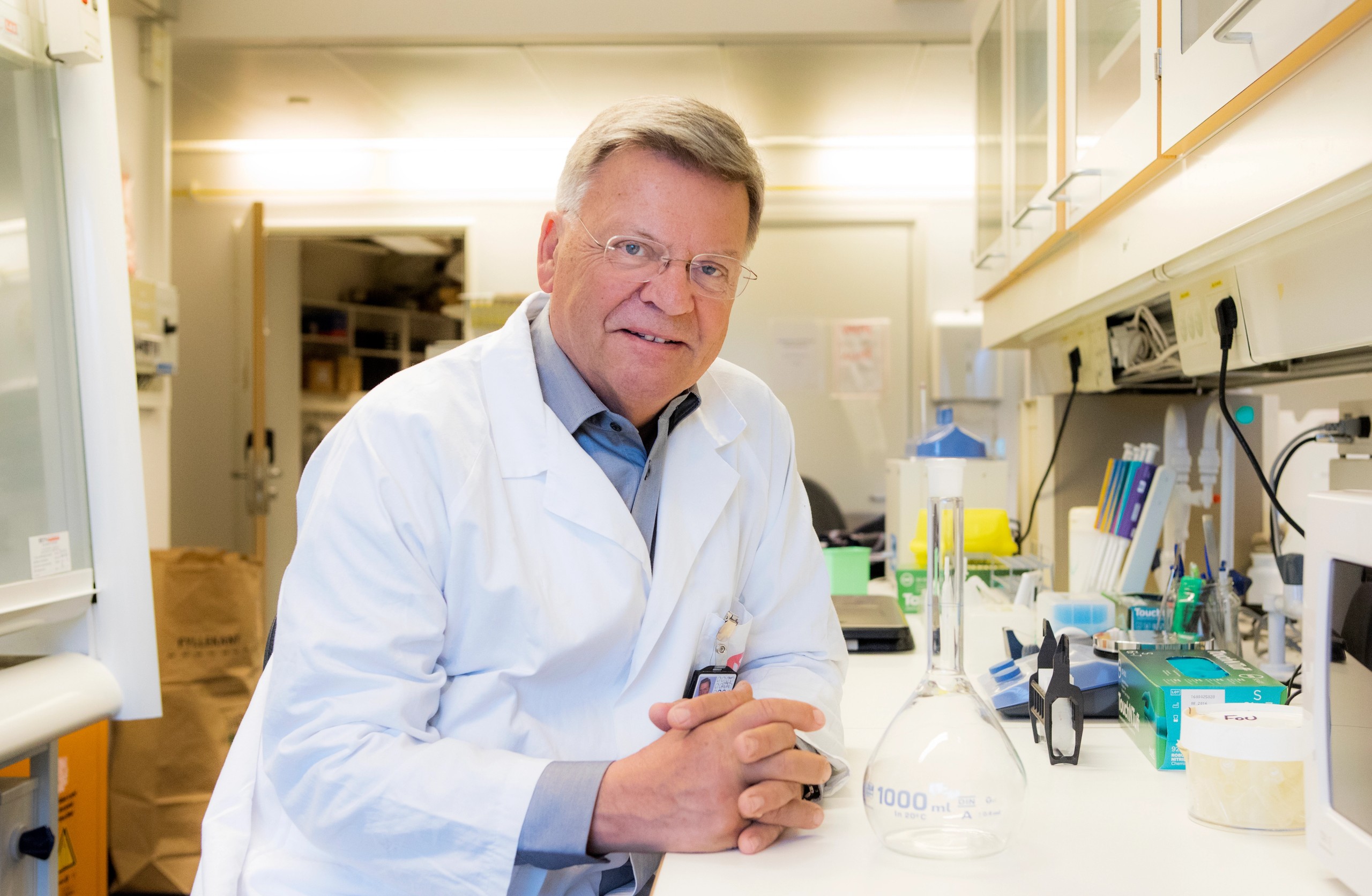 Foto av Torleiv Rognum. Han har labfrakk på seg, og sitter vendt mot kamera mens han lener seg på en laboratoriebenk.