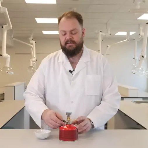 En mann i laboratoriefrakk gjør klar en gassbrenner.