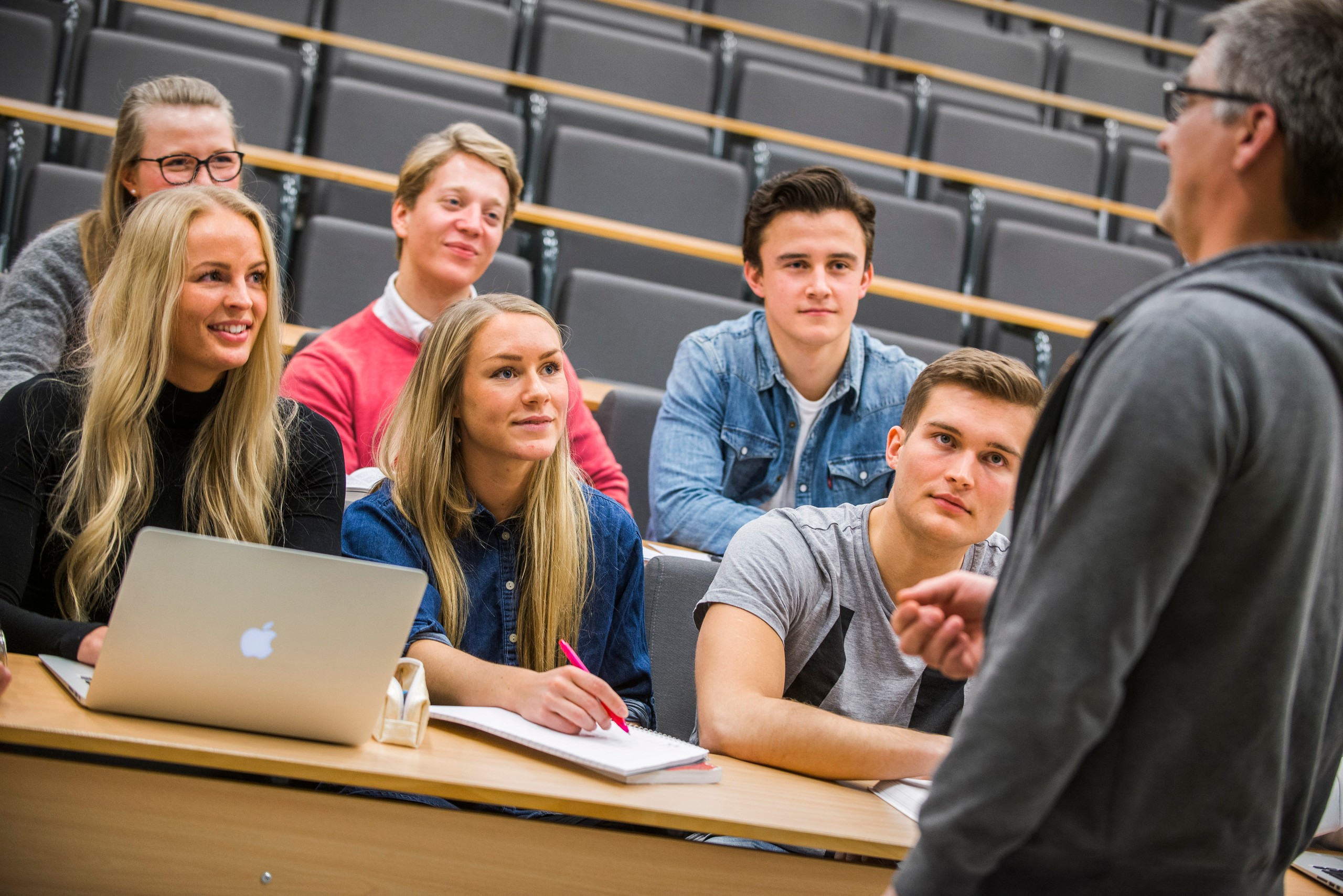 Foreleser som står i en forelesningssal og underviser foran studenter.