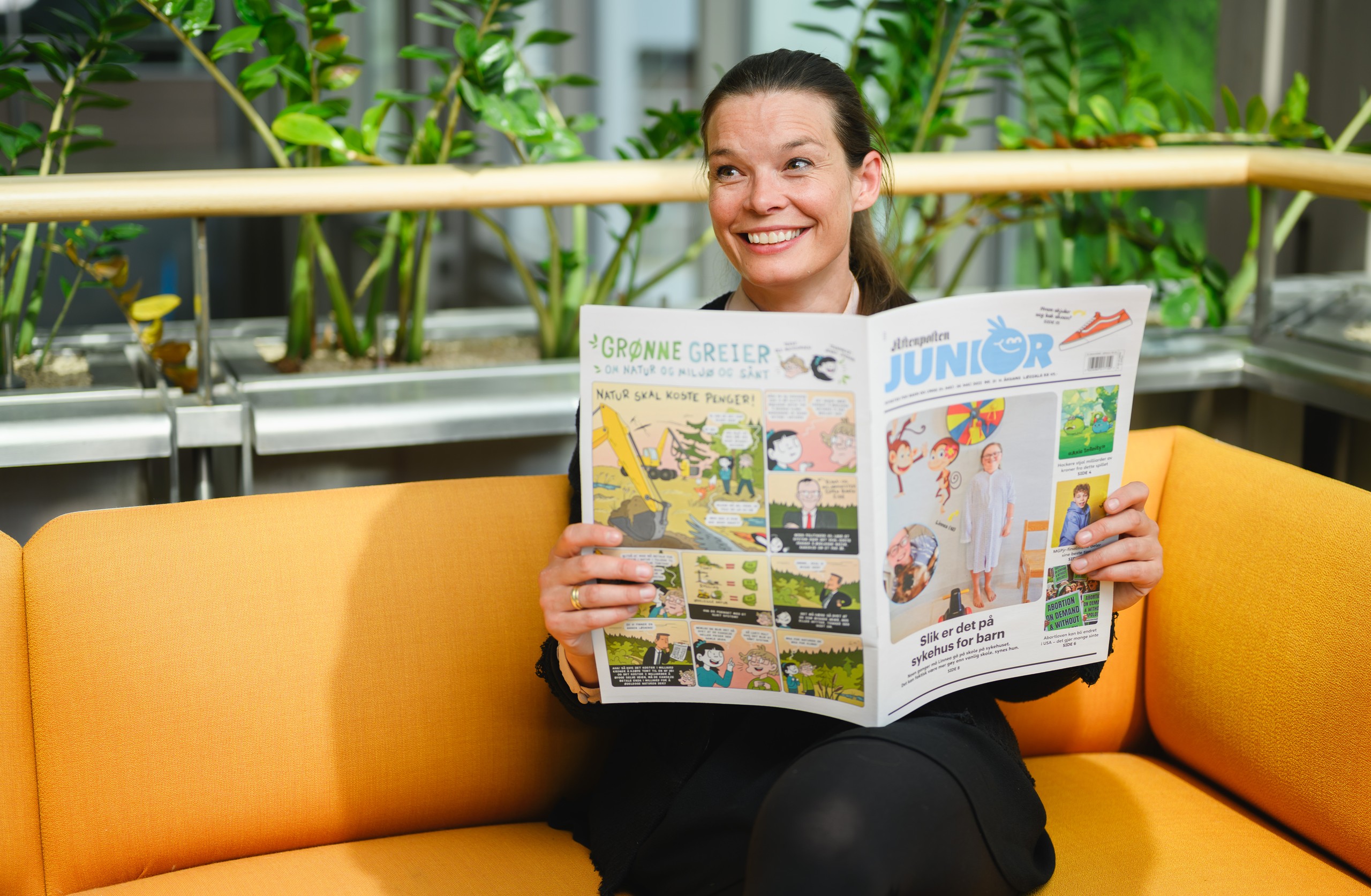 Mari Midtstigen, redaktør i Aftenposten Junior Skole, sitter på en sofa og holder opp ett eksemplar av Aftenposten Junior.