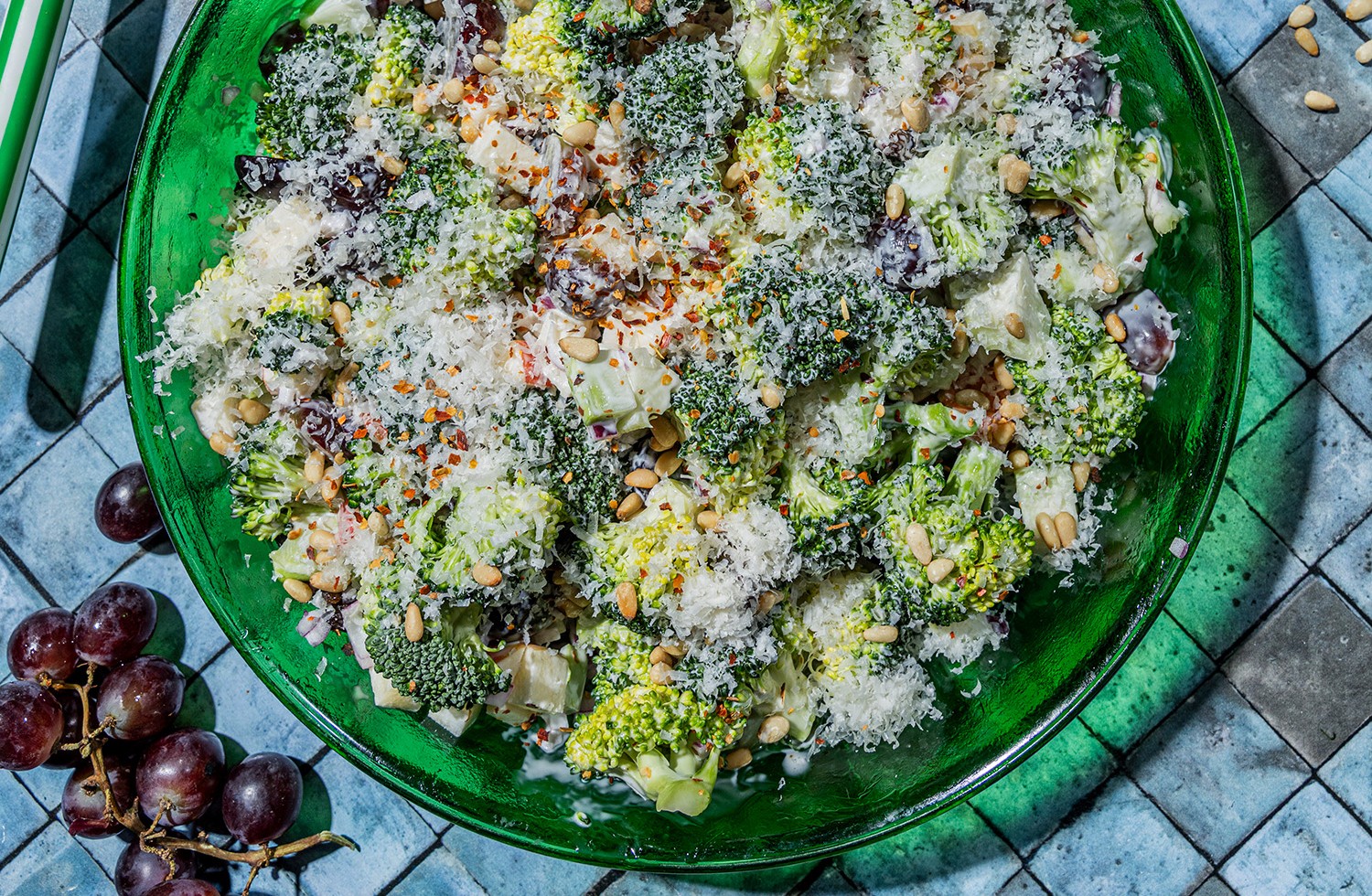 Fotografi av en bolle med brokkolisalat, med druer som ligger ved siden av bollen.