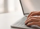 Close-up of hands typing on a laptop keyboard at a bright desk.