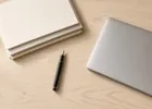Overhead view of neatly arranged document folders beside a pen and a laptop on a light wooden desk.