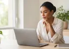An entrepreneur weighing options on her laptop in a sunlit home office.