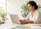 A freelance designer issuing an invoice from a laptop in a bright studio.