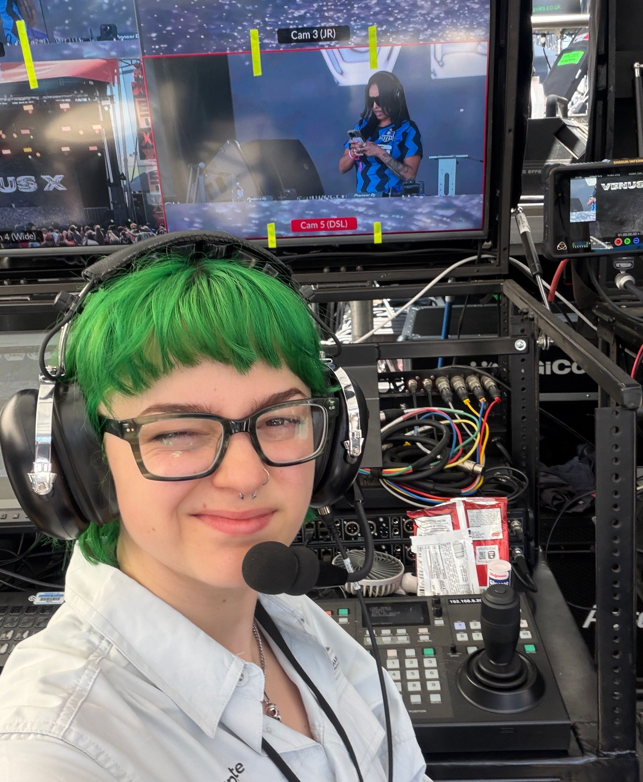 Emmy stands in front of a robocam control cart. She is wearing a comically large comms headset.