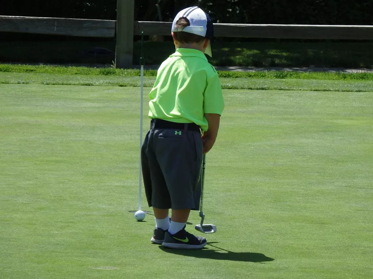 Kid with green polo practicing on the putting green