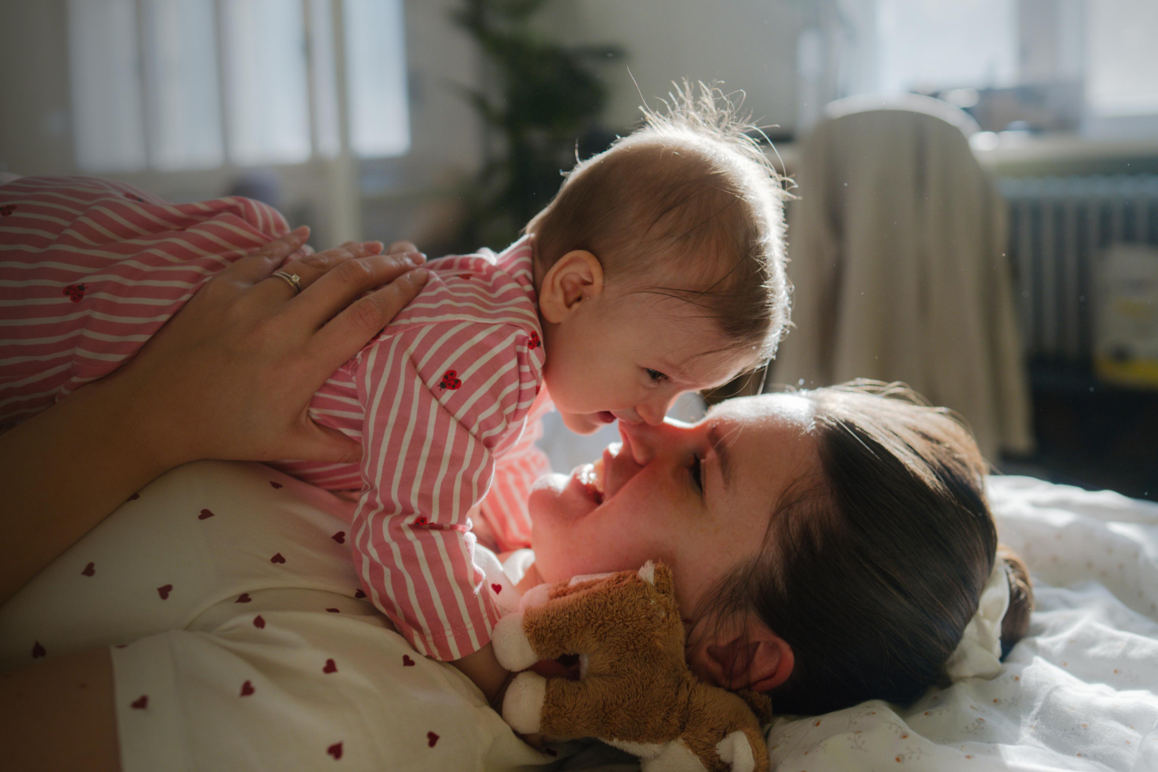 Mother and baby joyfully touching noses while lying down.