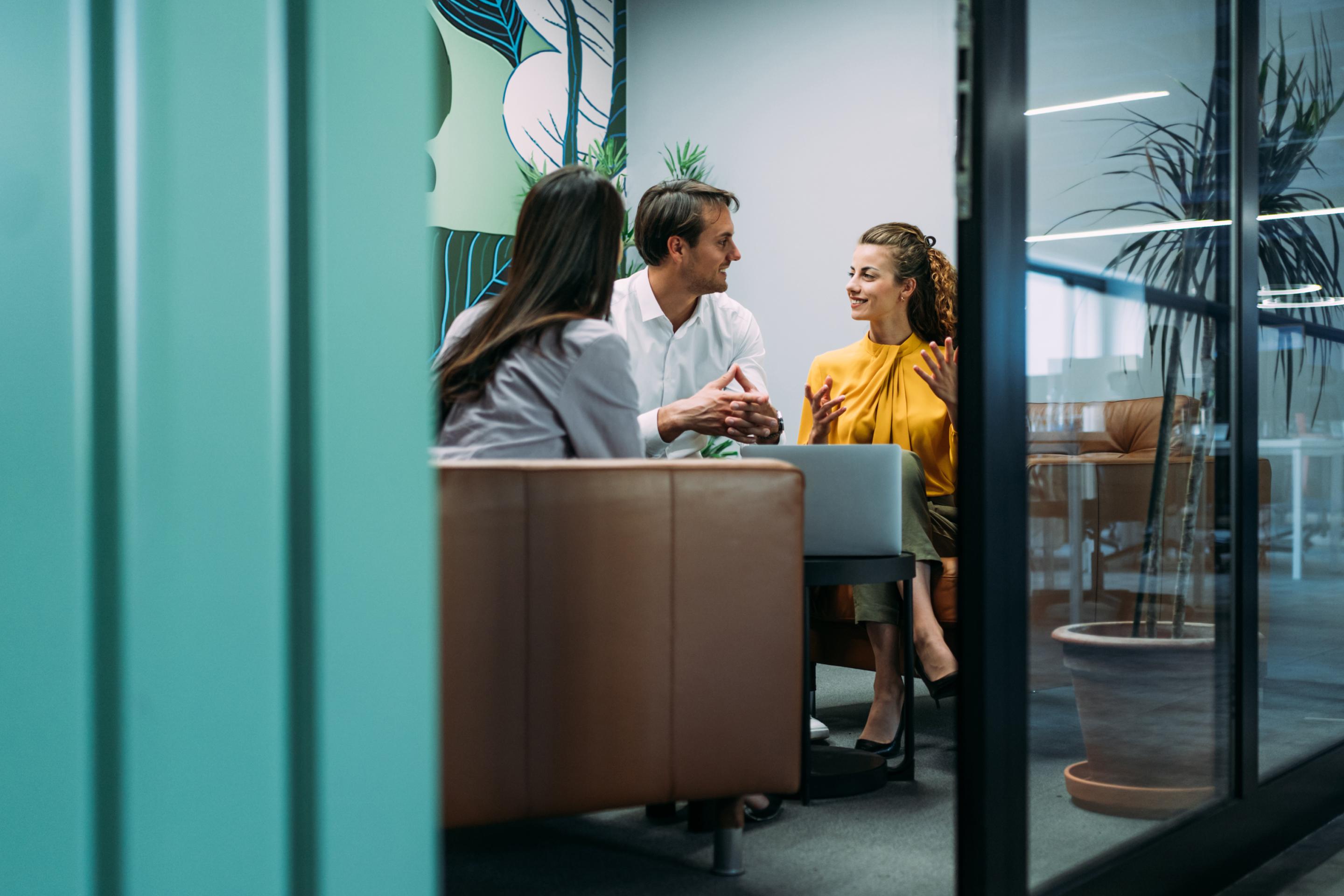 Three colleagues in a discussion at an office meeting room, representing an HR outsourcing team collaboration