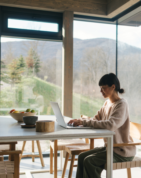 A smiling woman sits at a table and works on a laptop.