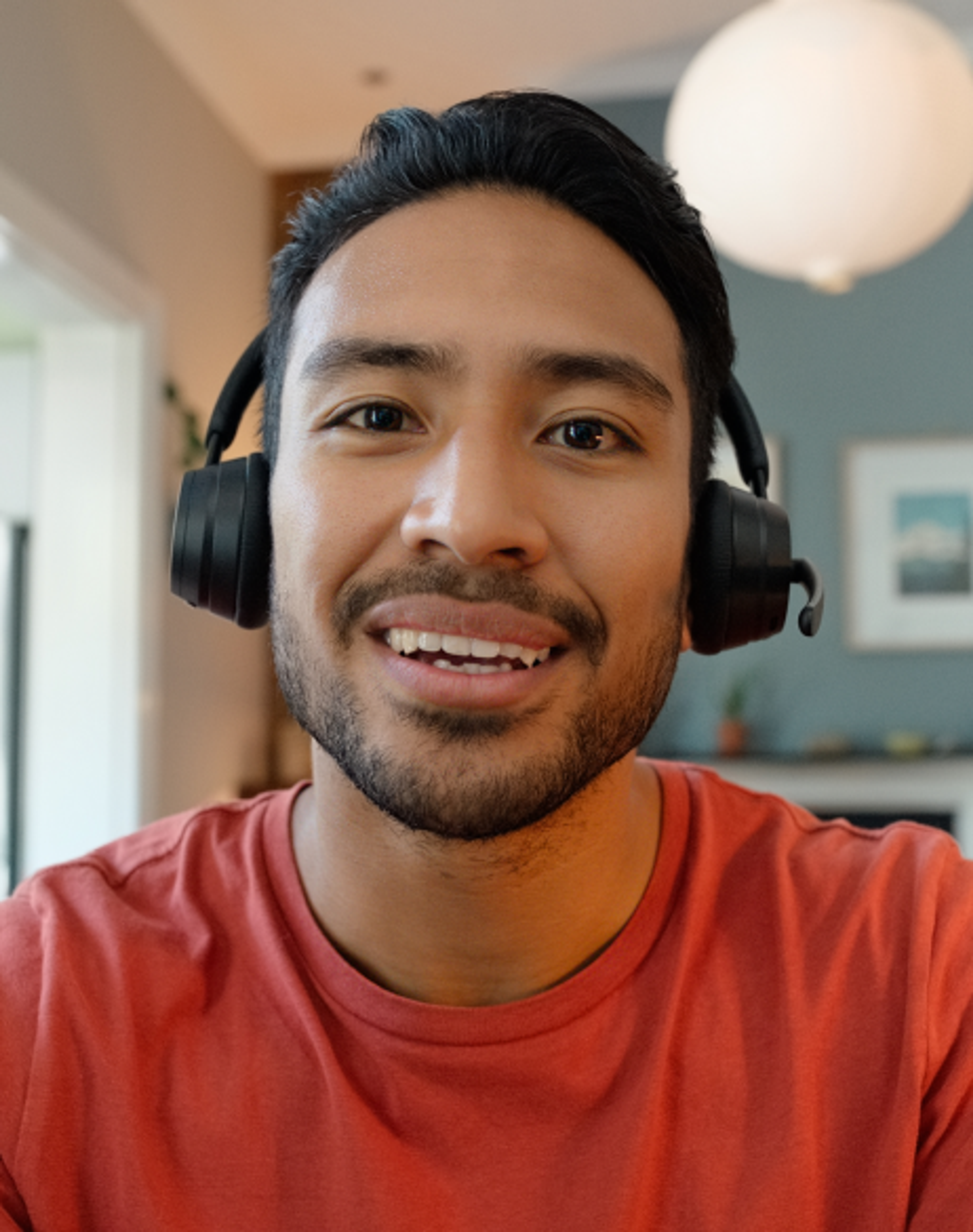 A smiling man with headphones sits across a table and makes eye contact.
