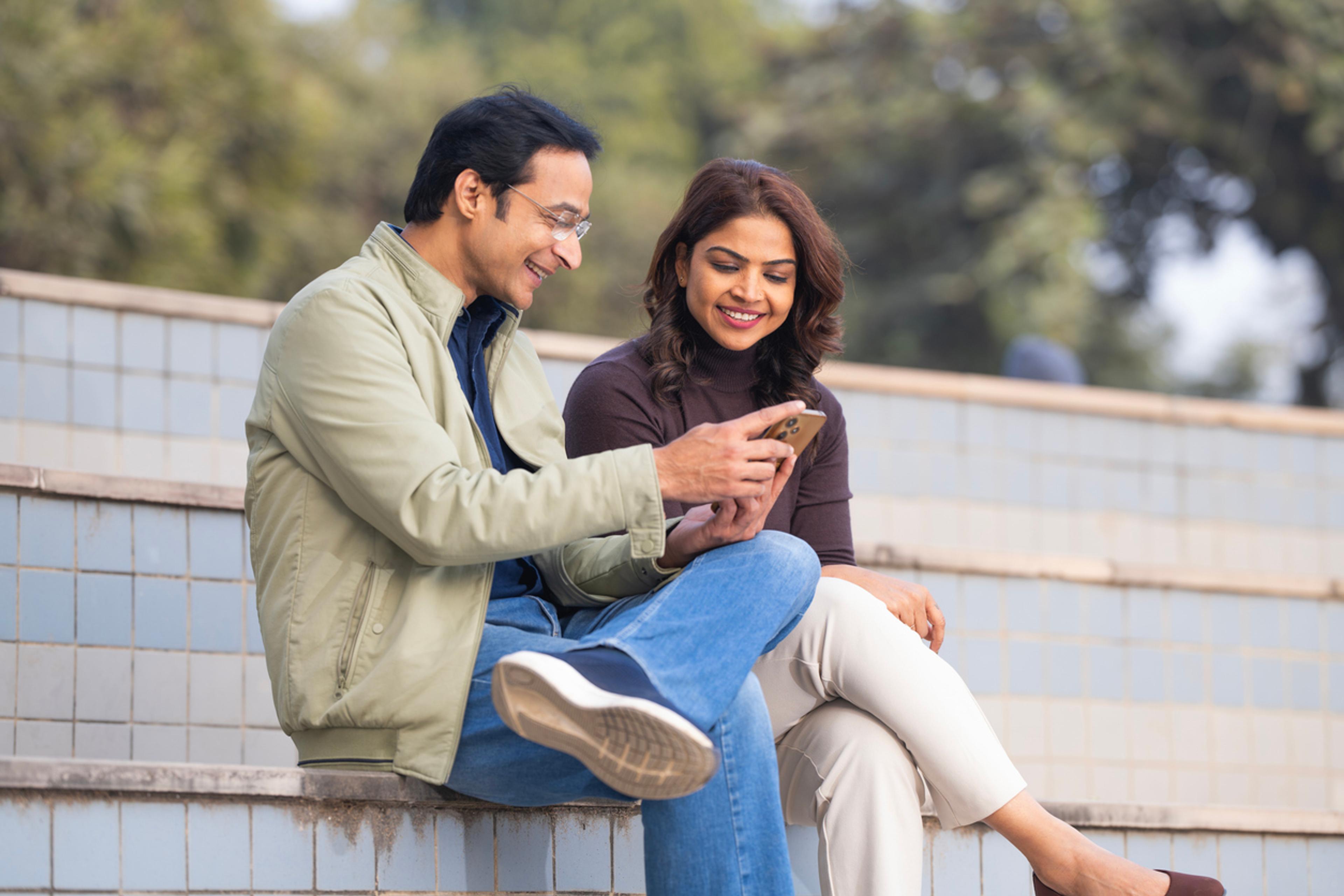 A couple using a phone while spending leisure time in a park in India