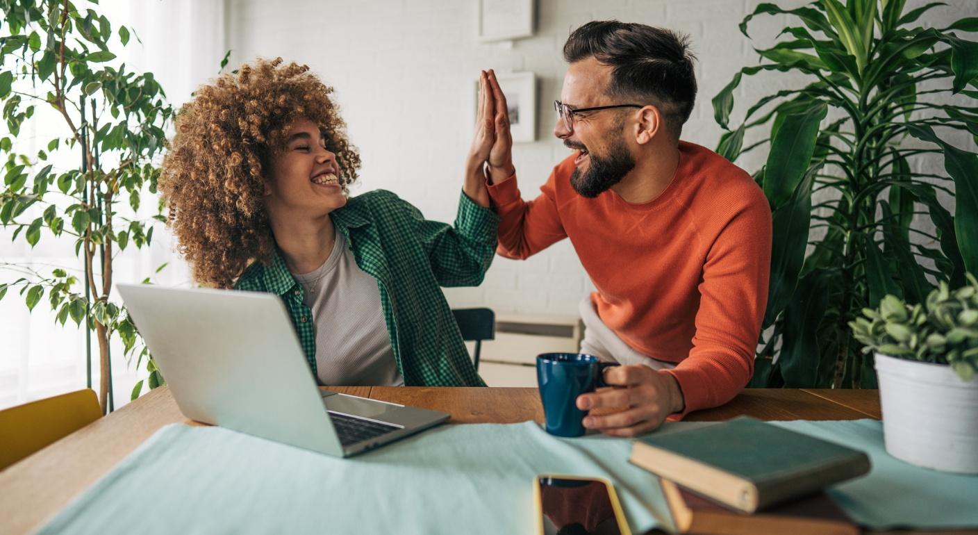 A smiling man and woman giving each other a high five at a desk with an open laptop.