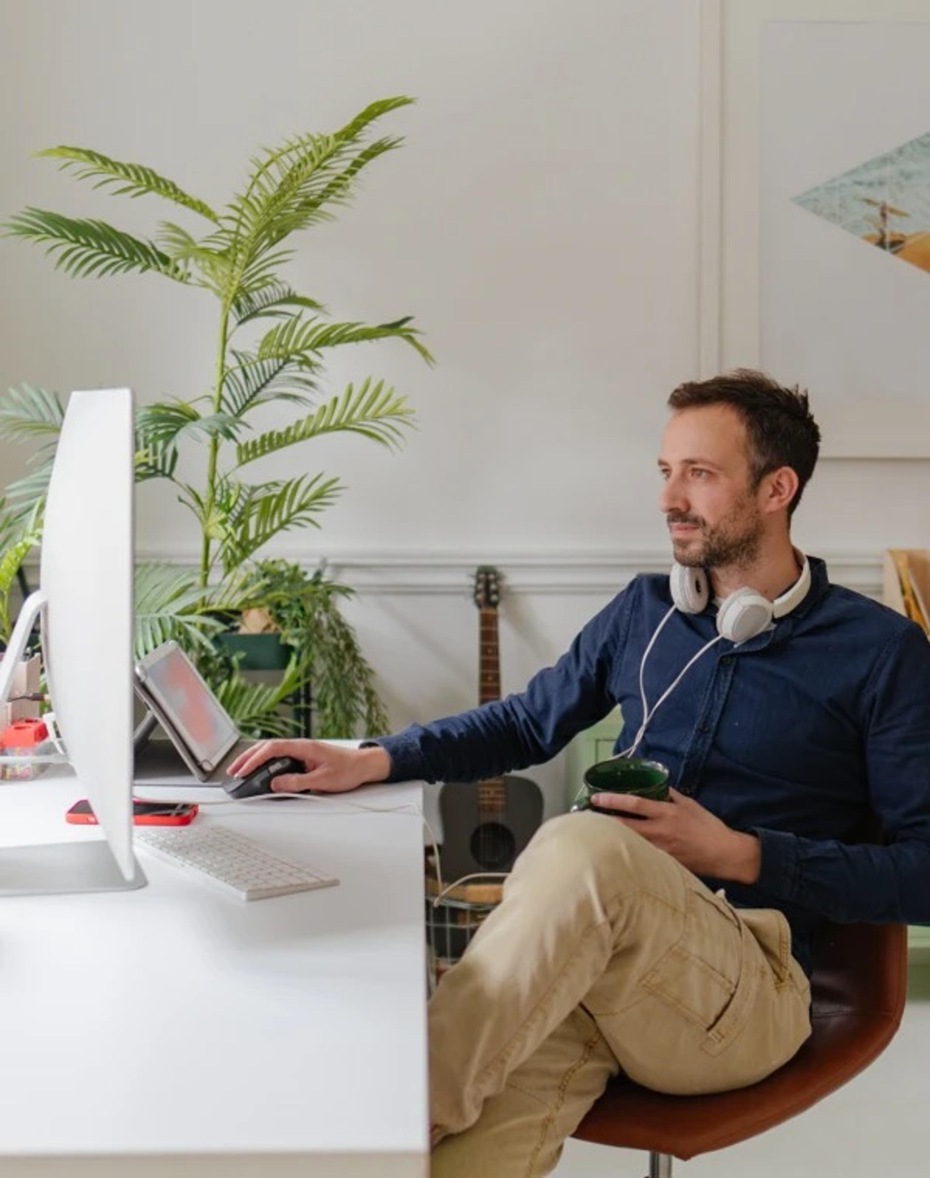 A content man sitting at a desktop computer using a computer mouse and holding a coffee mug.