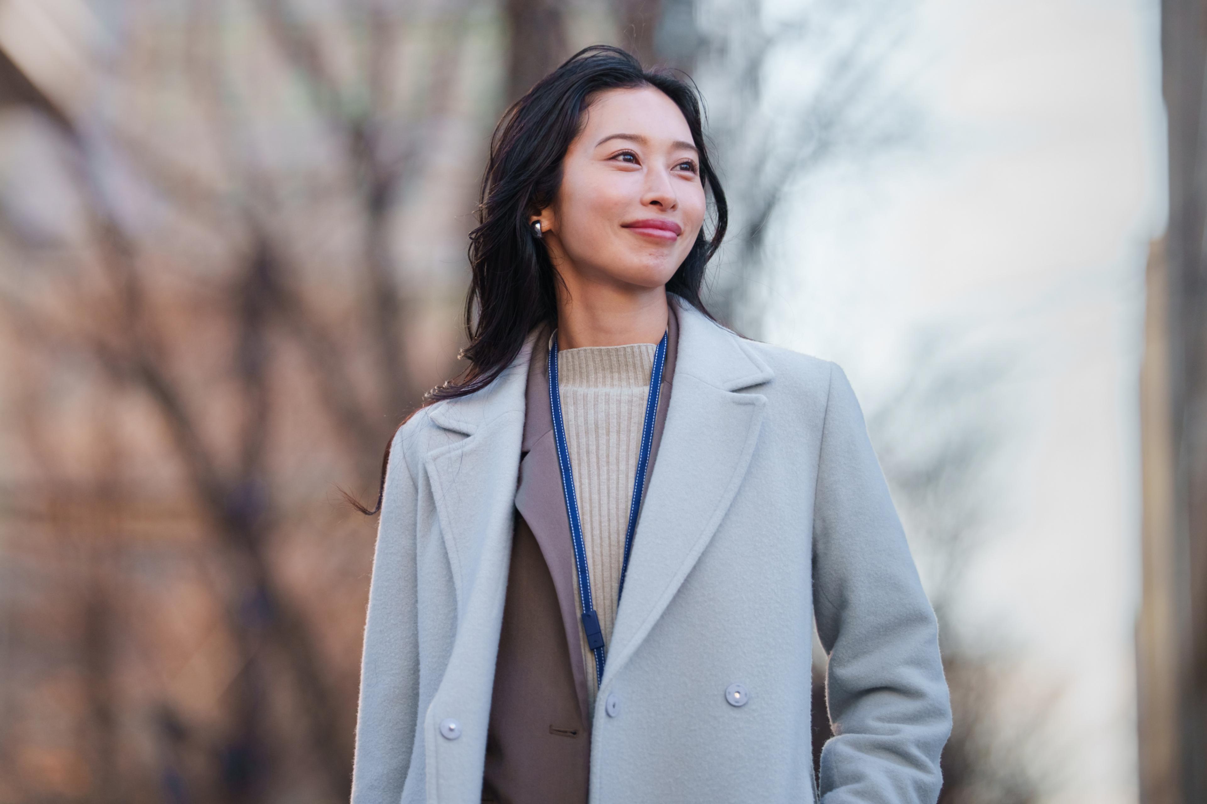 Smiling woman in a light blue coat looking up outdoors.