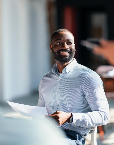 A smiling man in a striped button-down shirt holding papers during a meeting.