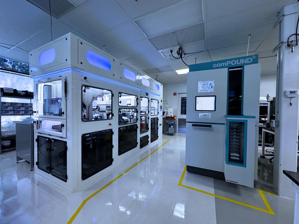 EditCo's automated CRISPR workcell: a row of enclosed liquid-handling stations beside a comPOUND sample store, in a laboratory marked out with floor tape