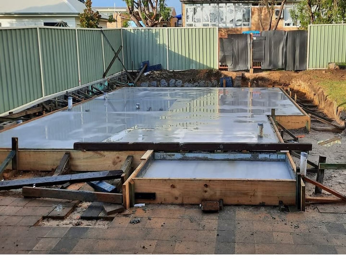 The finished slab inside its timber edge formwork, floated and curing, with the step-down landing boxed at the front