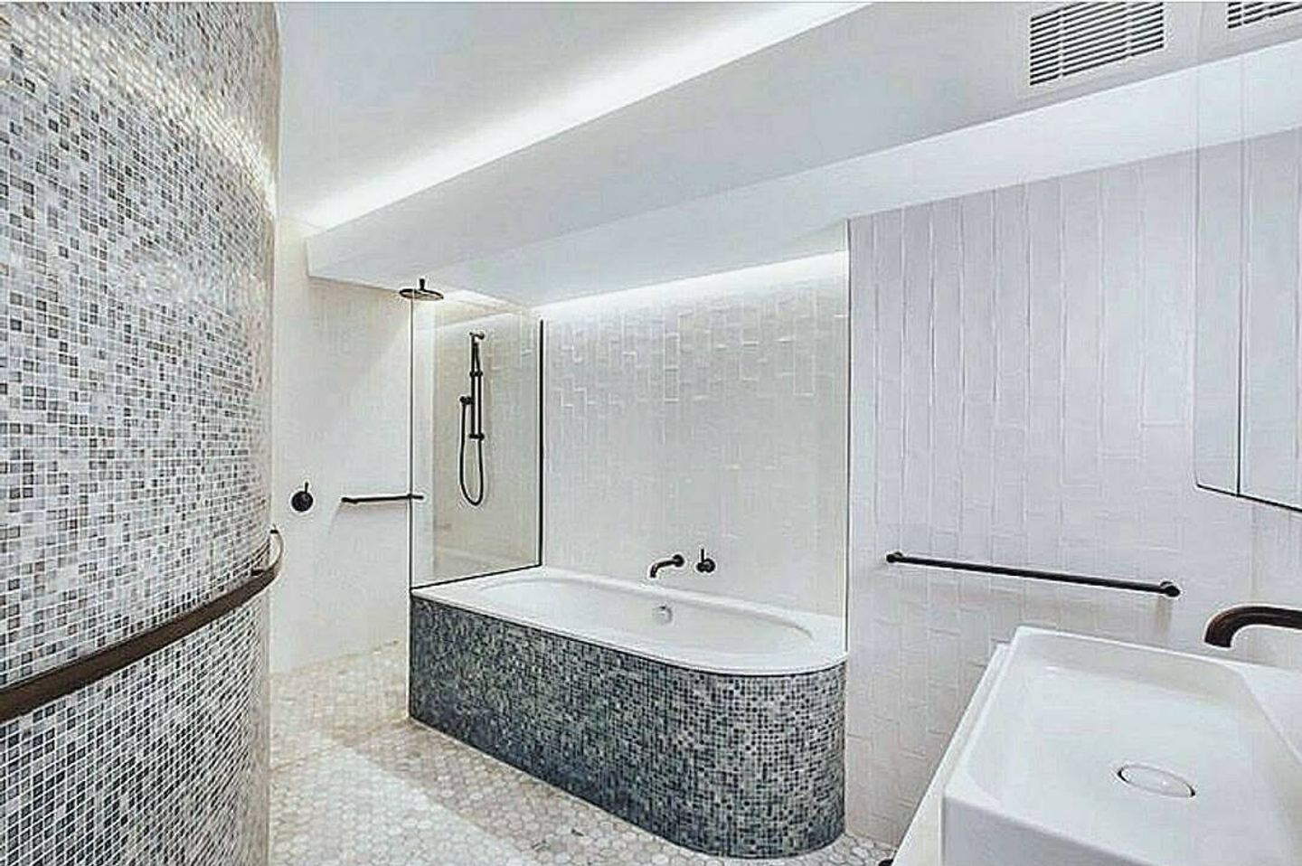A bath clad in mosaic tile set into a curved tiled wall beside a walk-in shower