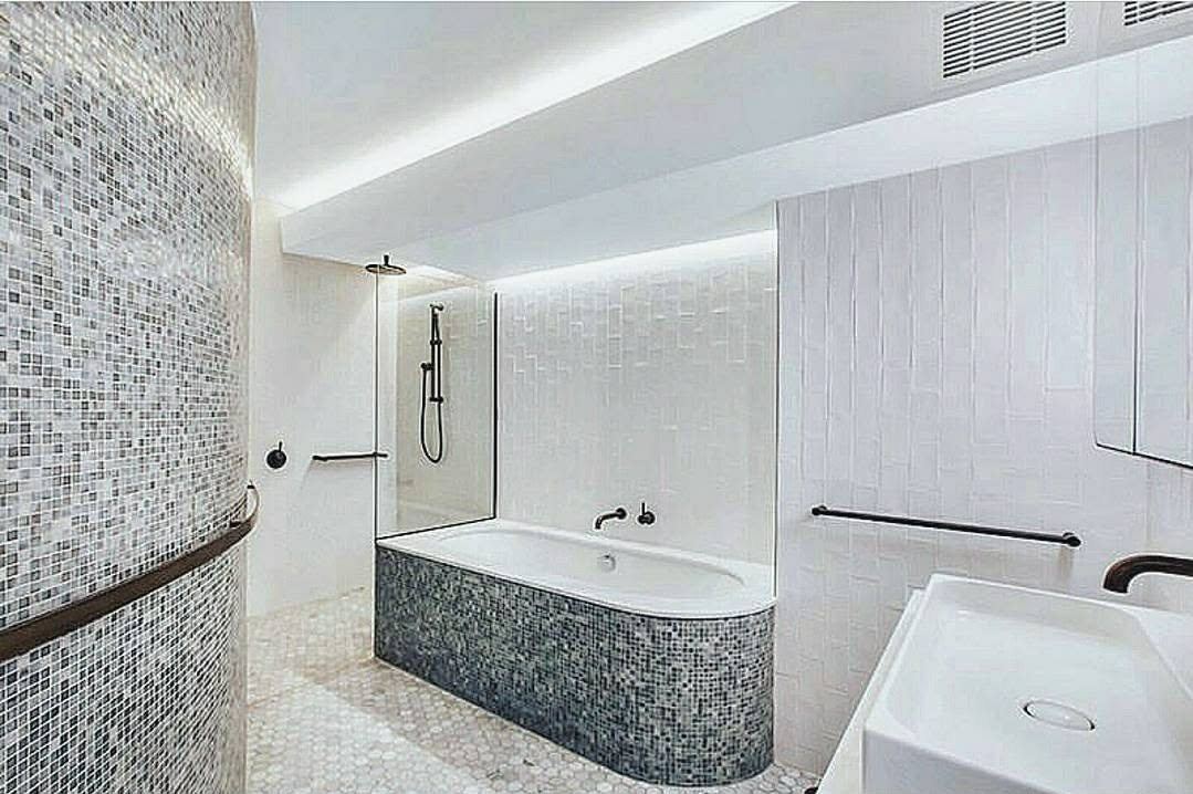 A bath clad in mosaic tile set into a curved tiled wall beside a walk-in shower