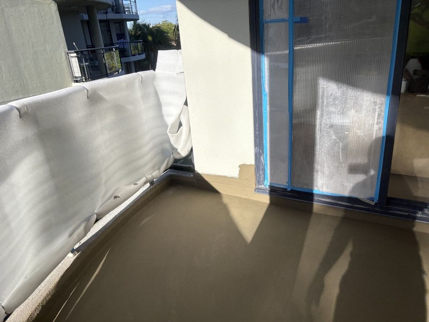 Waterproof membrane laid across a balcony slab with the balustrade sheeted for protection