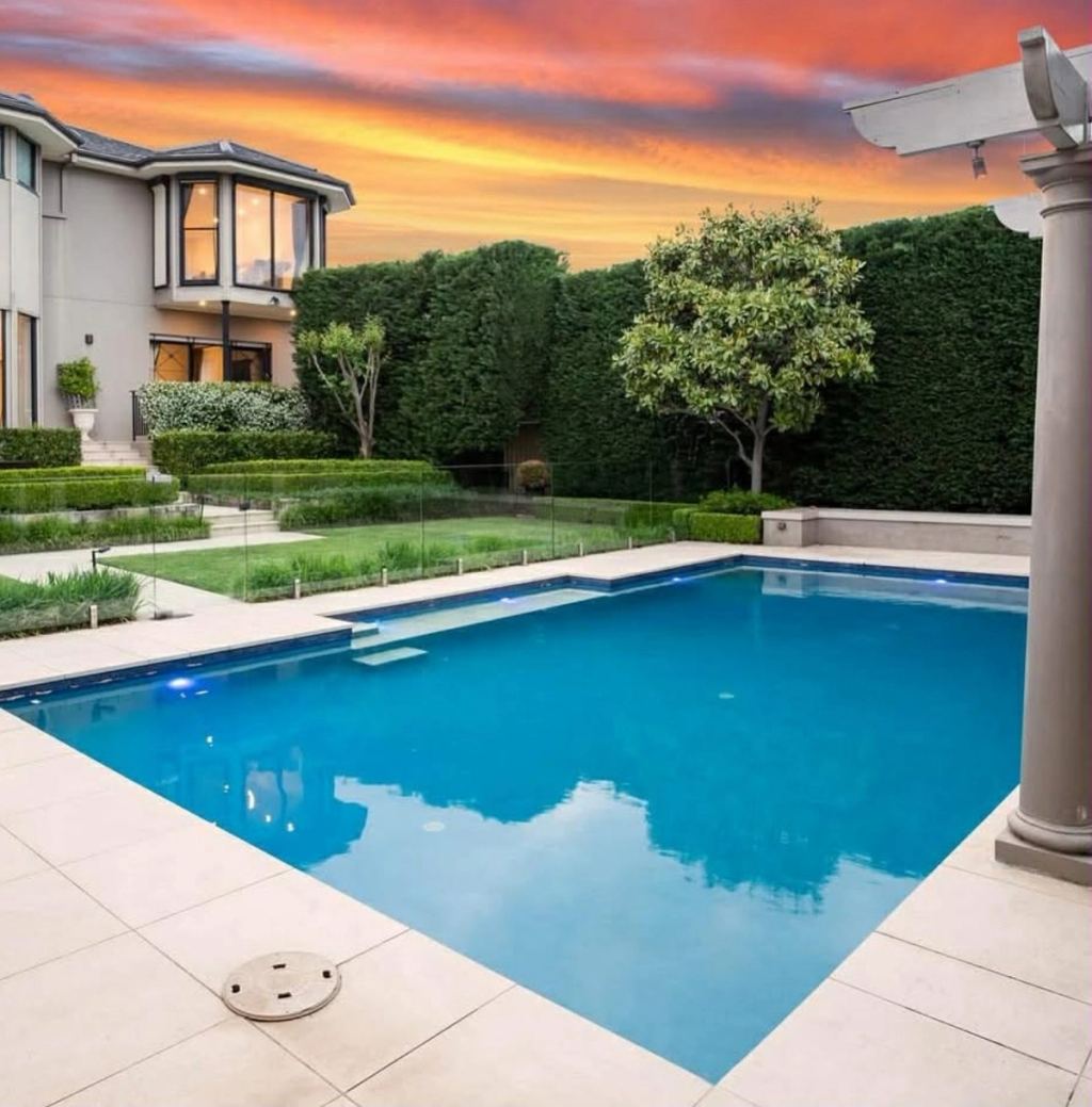 The Vaucluse residence and its pool terrace at sunset, seen across formal gardens