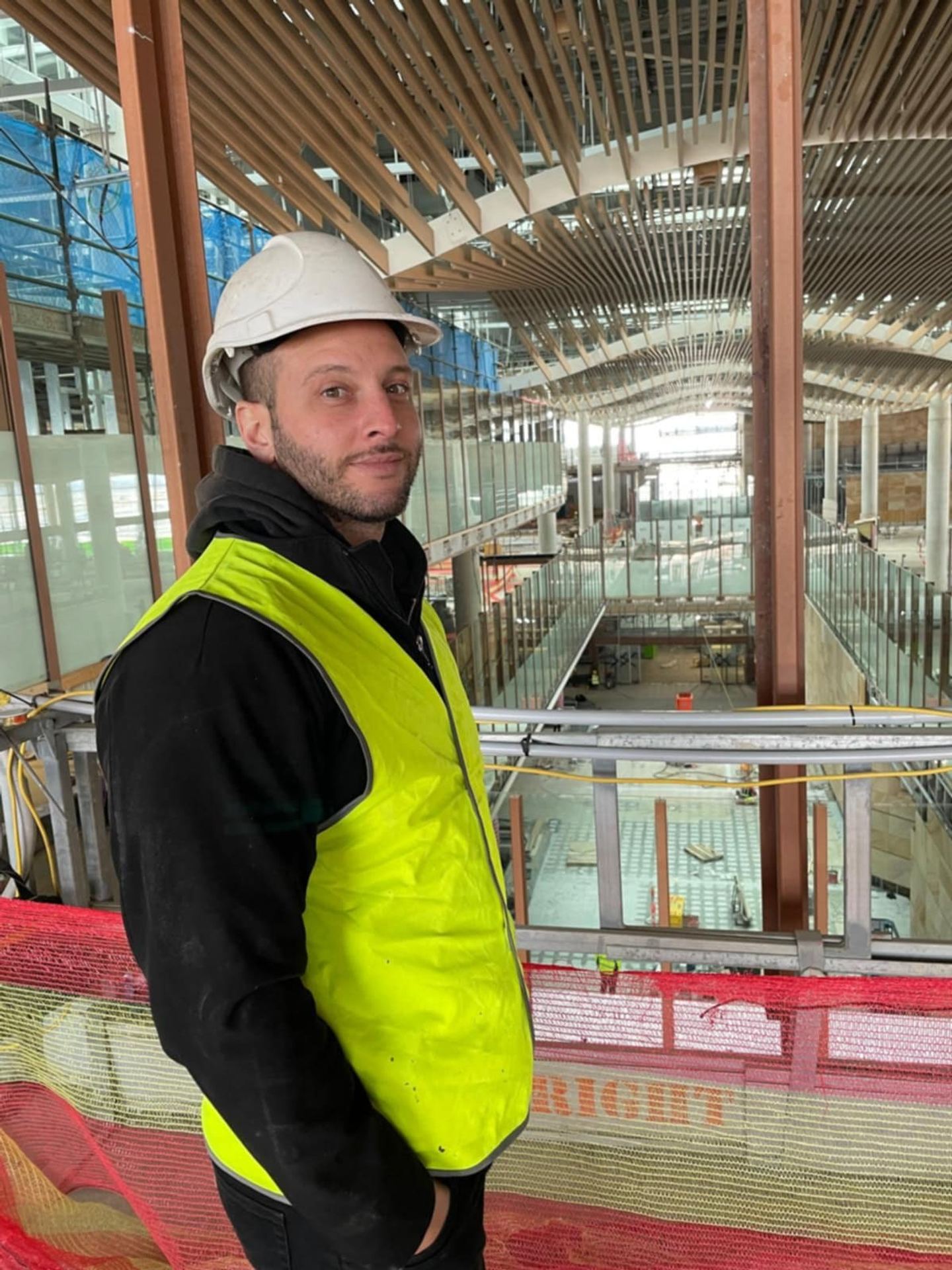 An HSRC project manager on site in hard hat and hi-vis, overlooking a commercial atrium under construction