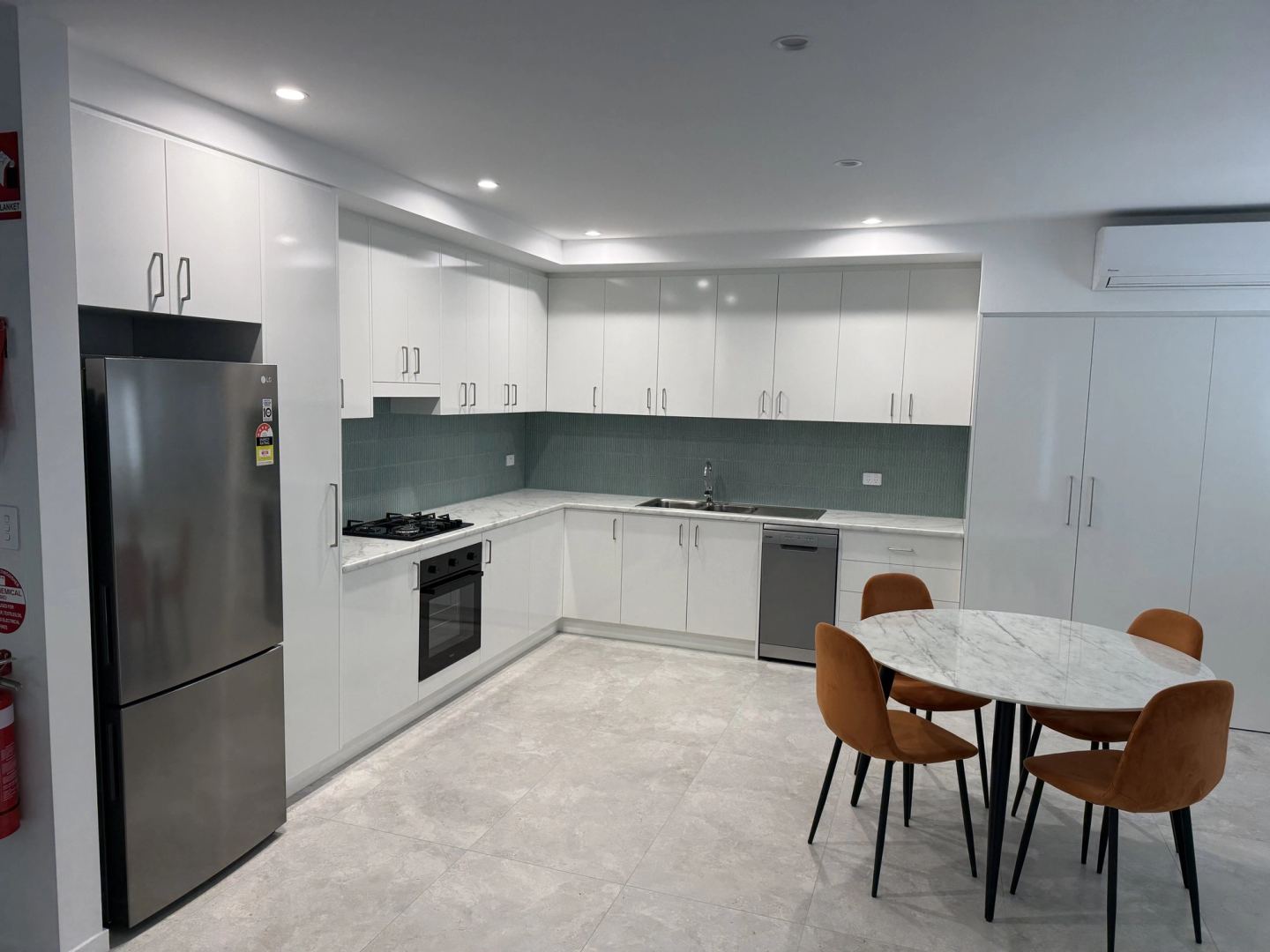 A completed apartment kitchen in white joinery with a green splashback and dining setting