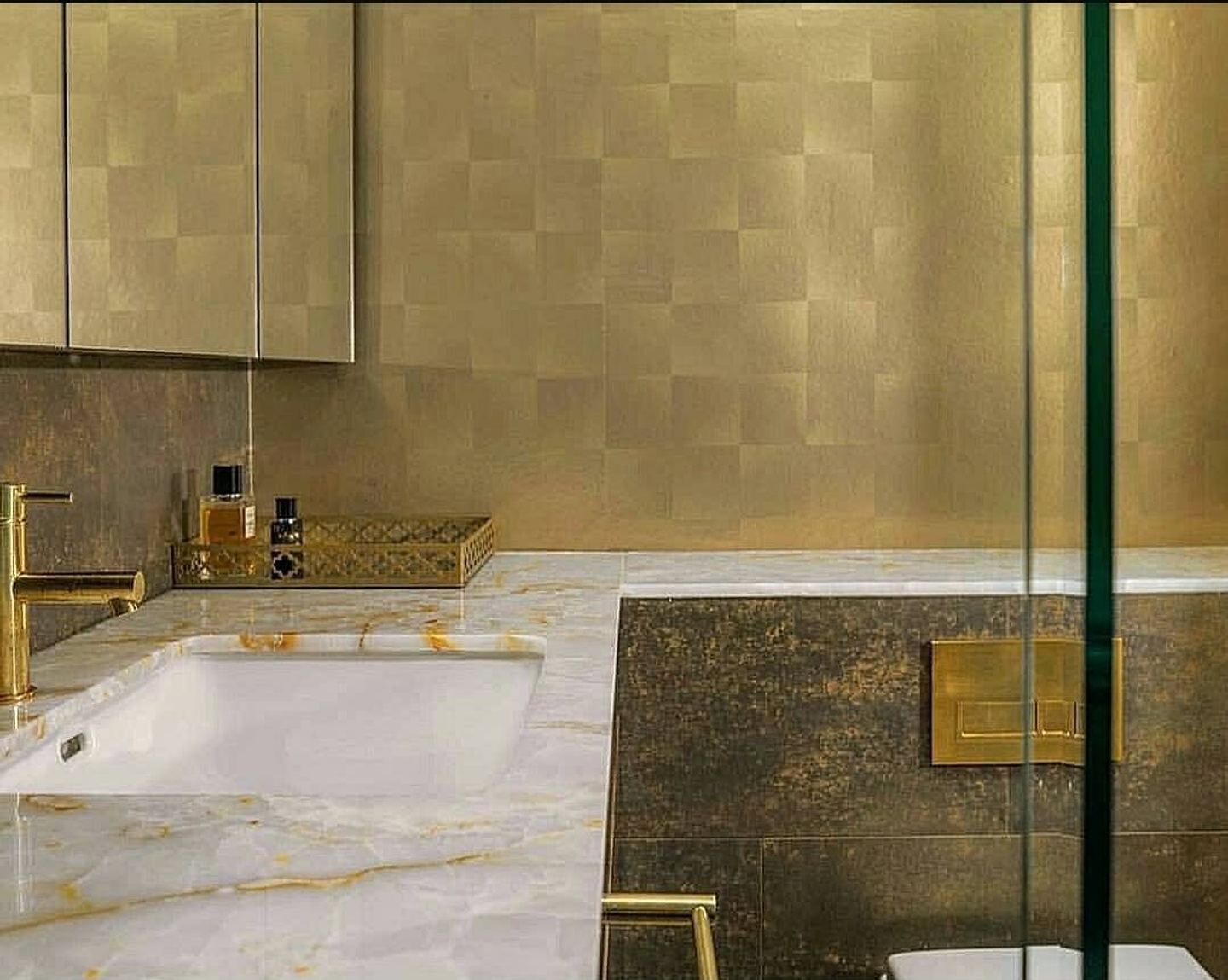 An ensuite in figured brass panelling and gold-veined marble around a set-in bath