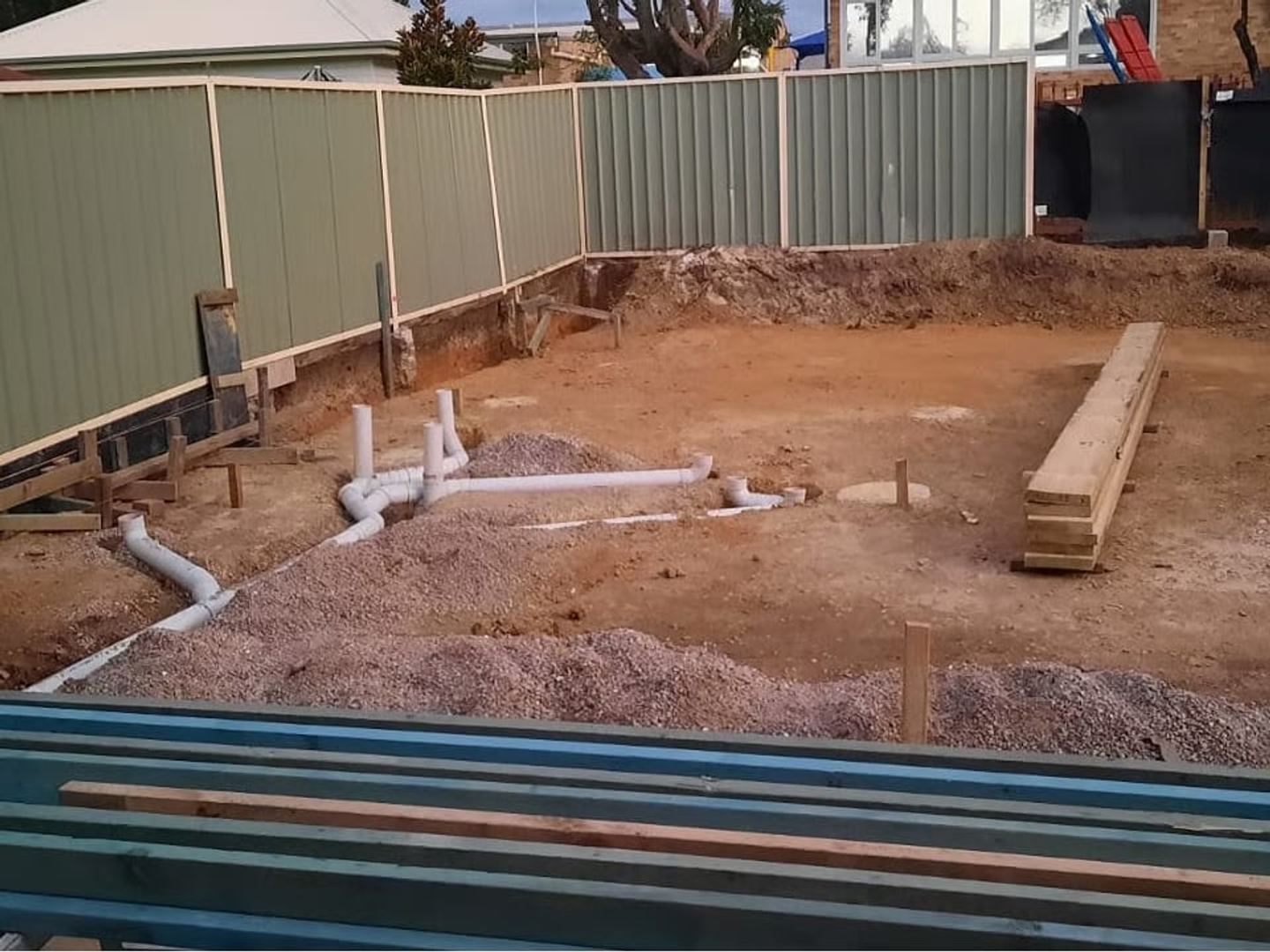 The rear yard excavated and levelled, with stormwater and sewer pipework set out across the pad before the slab