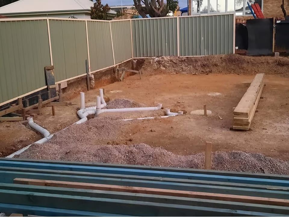The rear yard excavated and levelled, with stormwater and sewer pipework set out across the pad before the slab