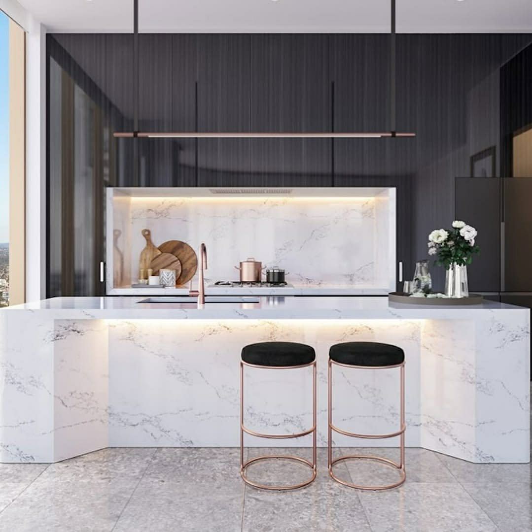 A marble kitchen with a waterfall island, brushed brass tapware and concealed lighting