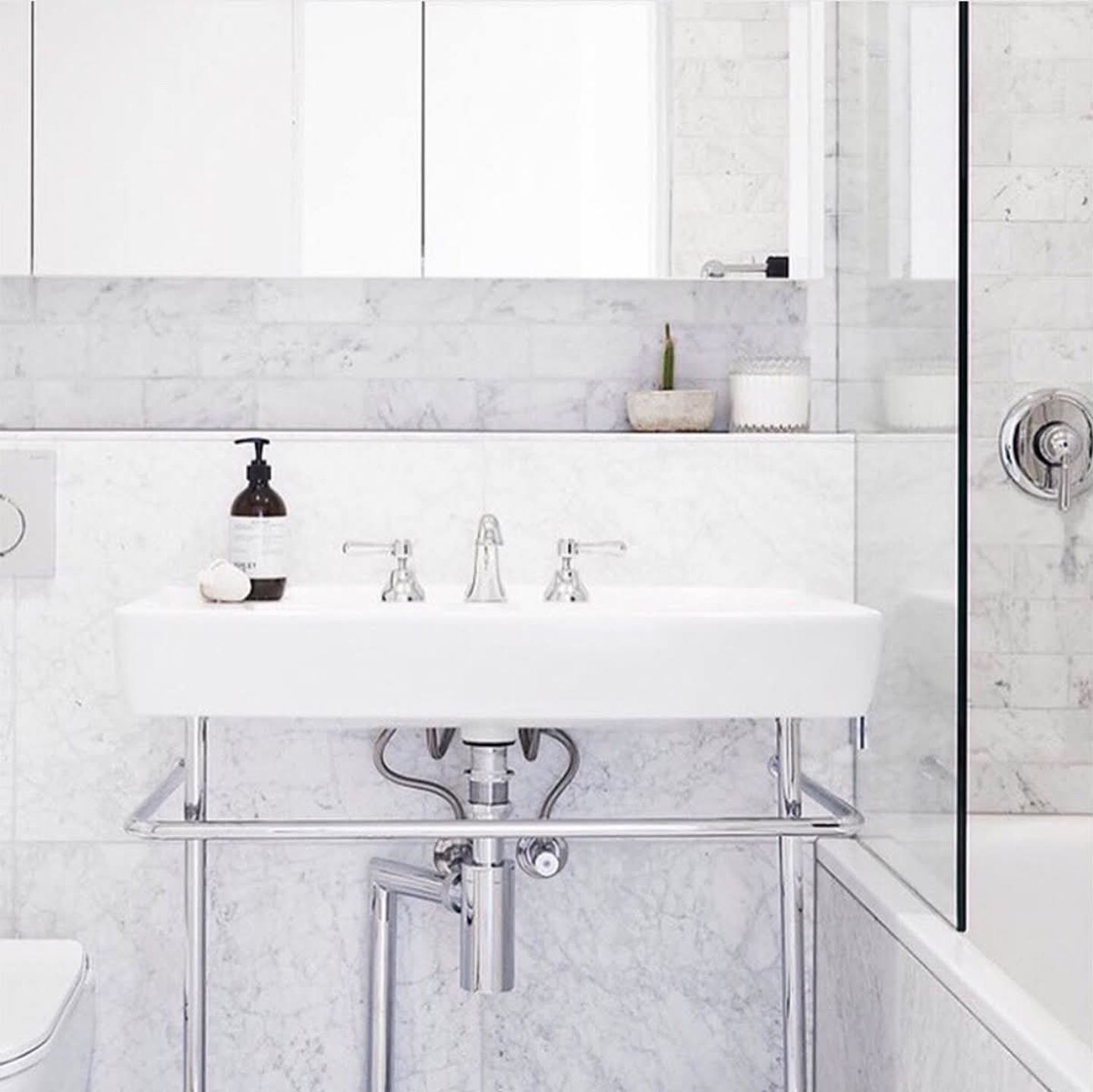 A console basin in marble and polished chrome beneath a mirrored cabinet