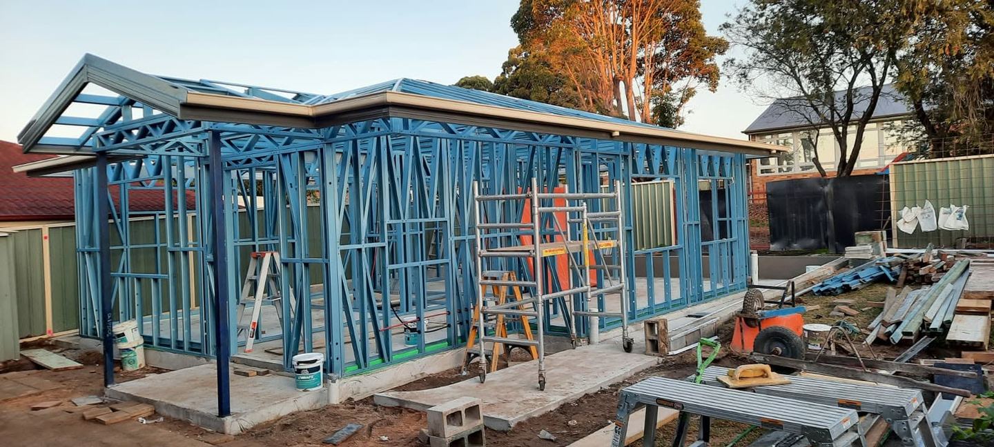 The light-gauge steel frame standing on the completed slab with the roof structure fixed and openings framed