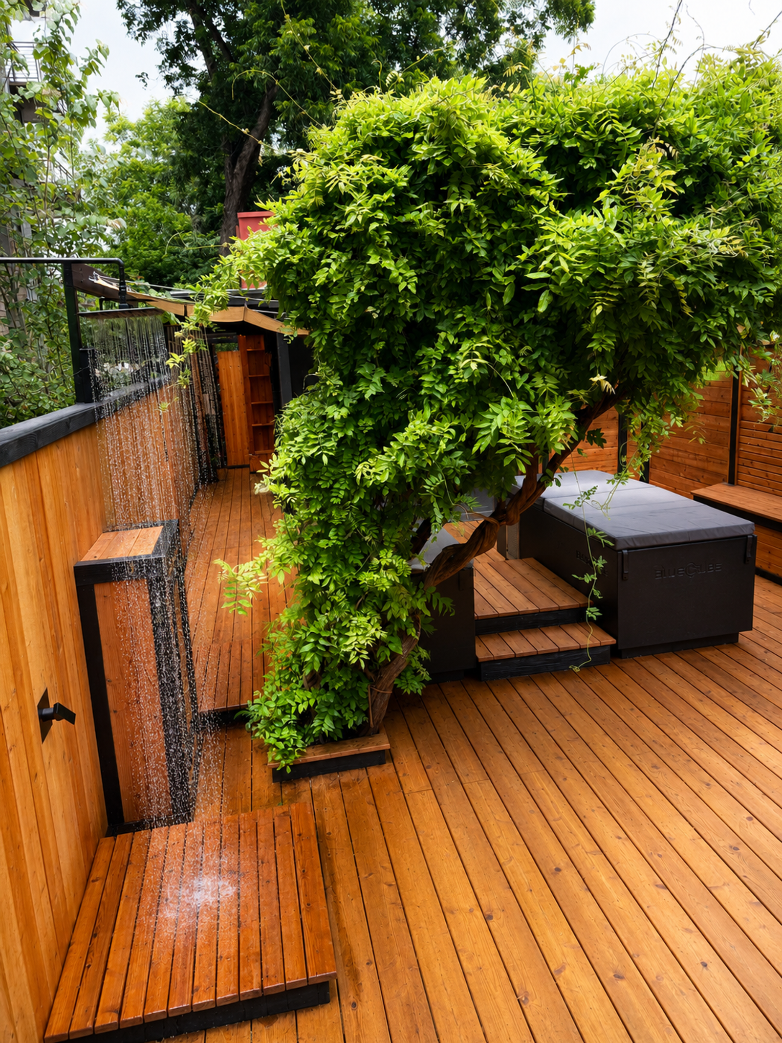 A luxurious outdoor wooden deck features a running shower, a large green tree, and an integrated dark hot tub with steps.