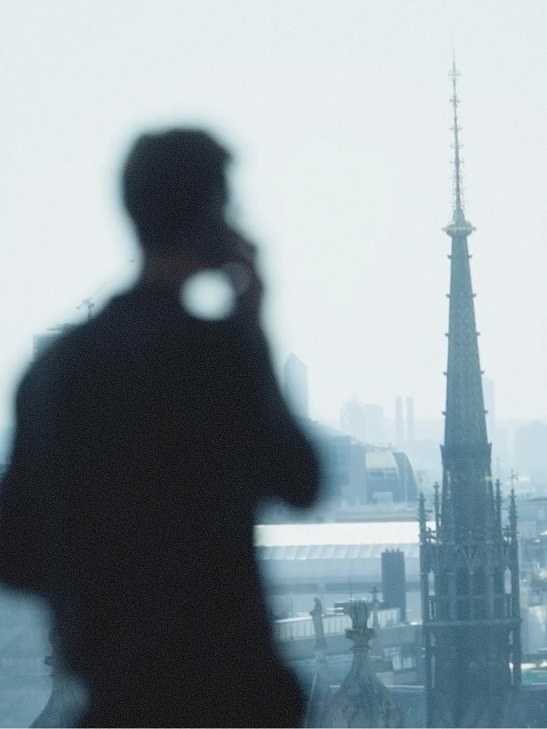 An image of a man looking through a window. The window shows a foggy day and a gothic church. 