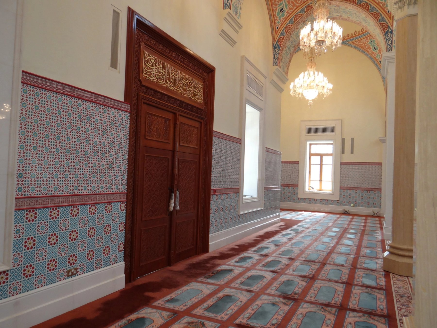 Mosque interior passage with carved timber door, tiled walls and chandeliers