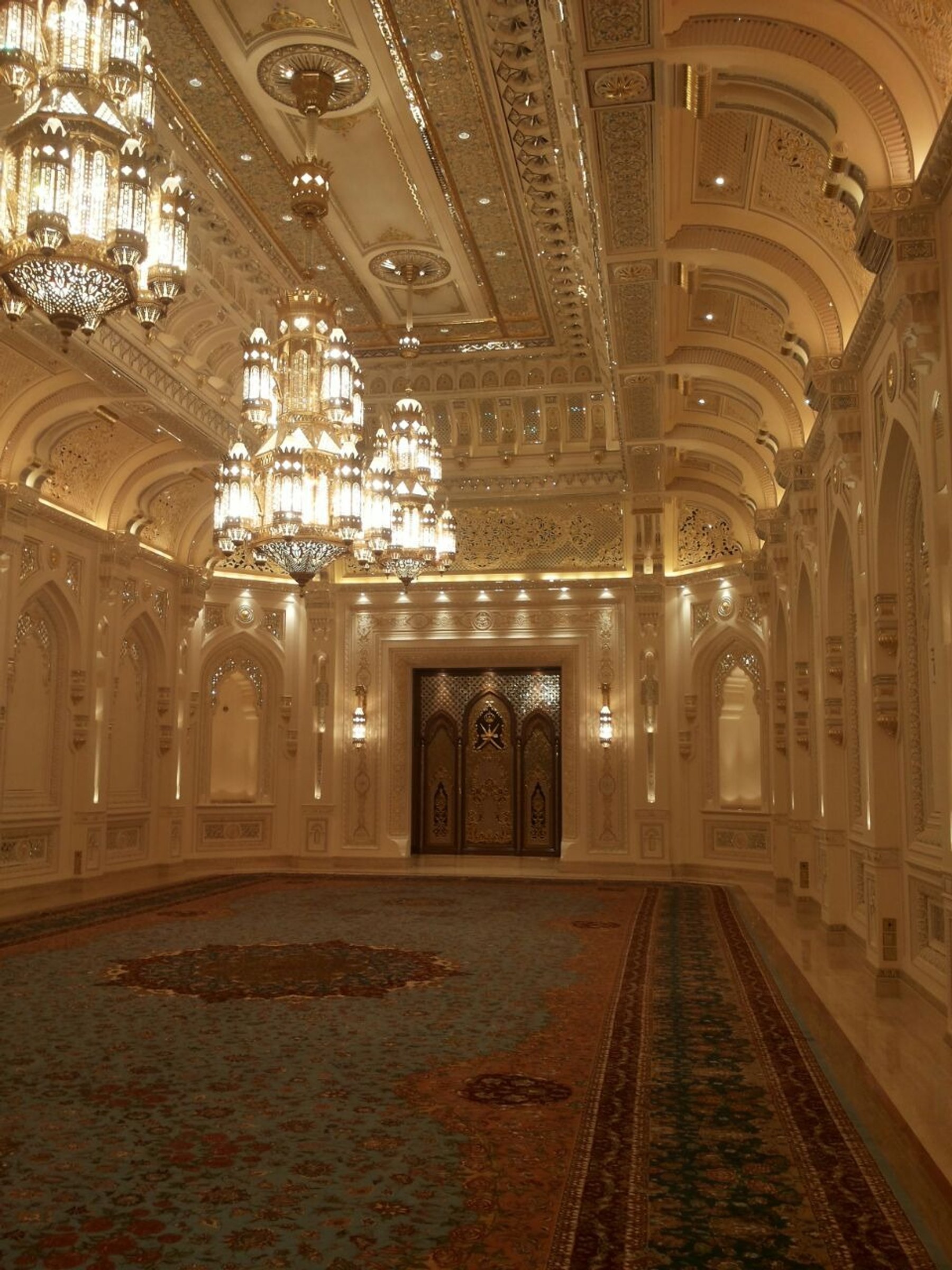 Long formal hall with chandeliers, patterned carpet and ornate wall detailing