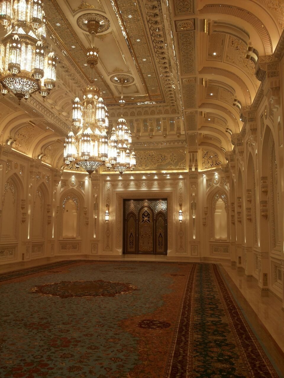Long formal hall with chandeliers, patterned carpet and ornate wall detailing